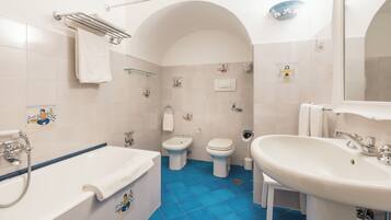 Een badkamer met een bad, wastafel en twee toiletten.