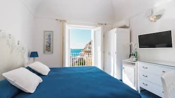 A bedroom with a bed, a dresser, a TV, and a view of a balcony with a cityscape.