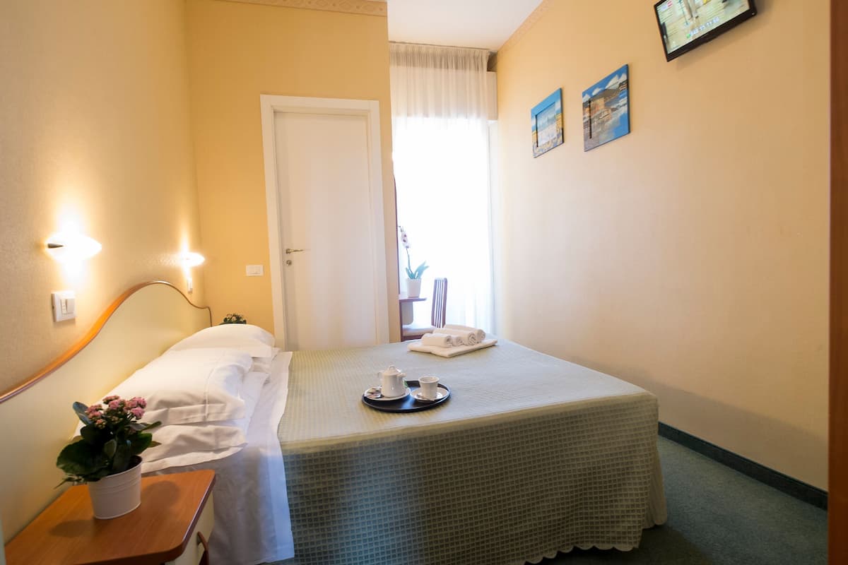 A neatly made bed with a tray of tea and a white towel, a small table with a potted plant, and a door leading to another room.