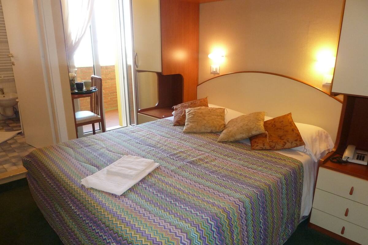 A neatly made bed with a patterned bedspread, a bedside lamp, and a nightstand with a phone.