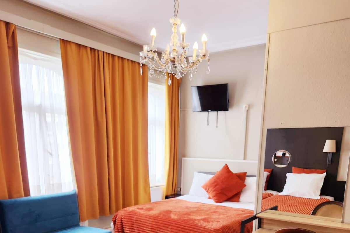 Une chambre d’hôtel avec deux lits, un bureau, une chaise, une télévision et un lustre.