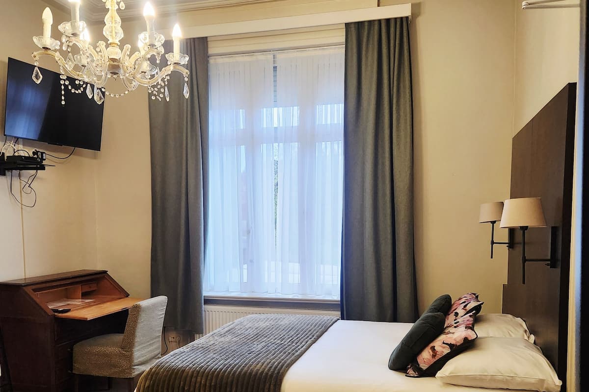 Une chambre d’hôtel avec un lit, un bureau, une télévision et un lustre.