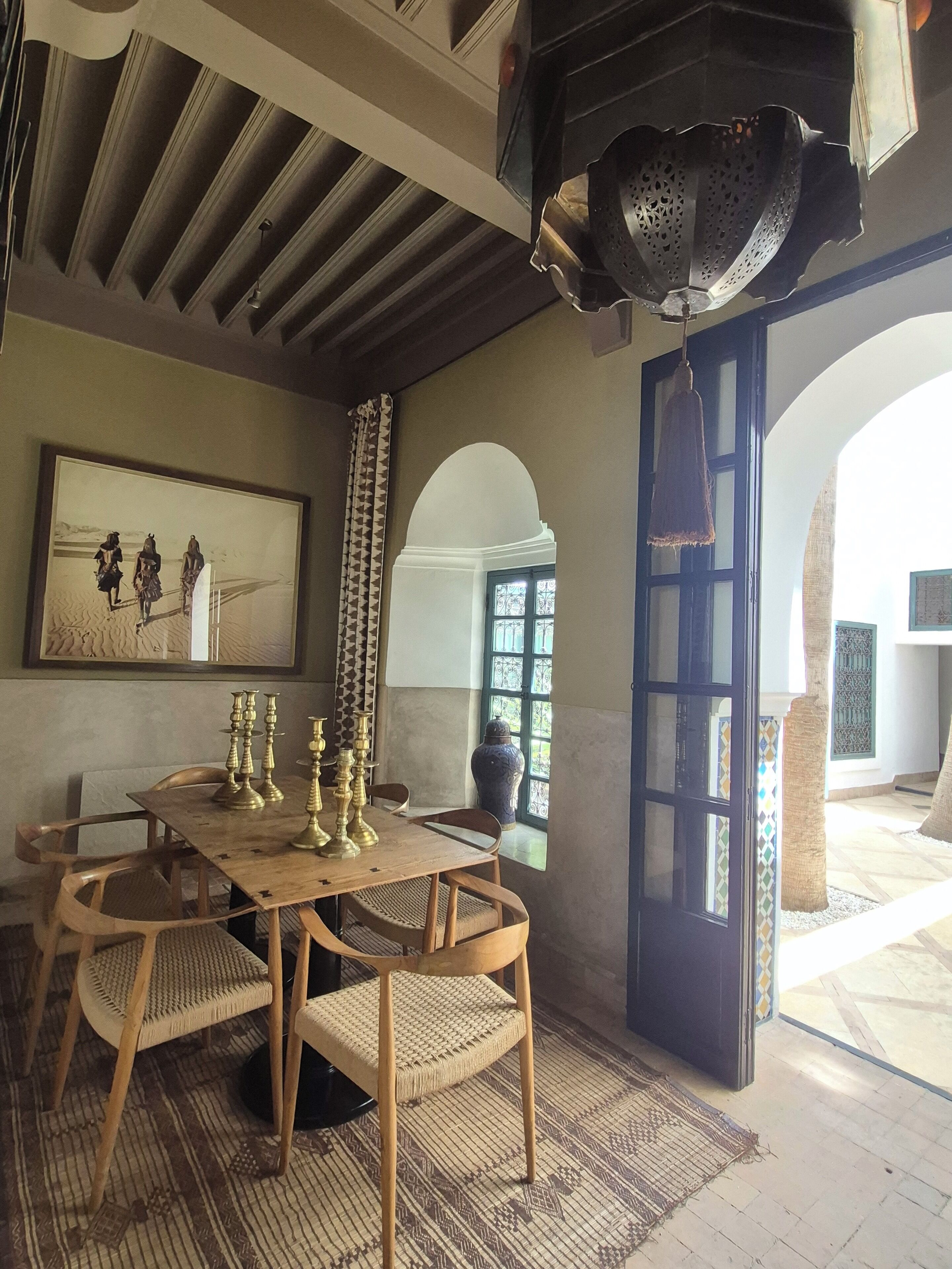 Un coin repas avec une table en bois dressée pour quatre personnes, entourée de chaises en osier. Un grand vase et des chandeliers en laiton sont posés sur la table.