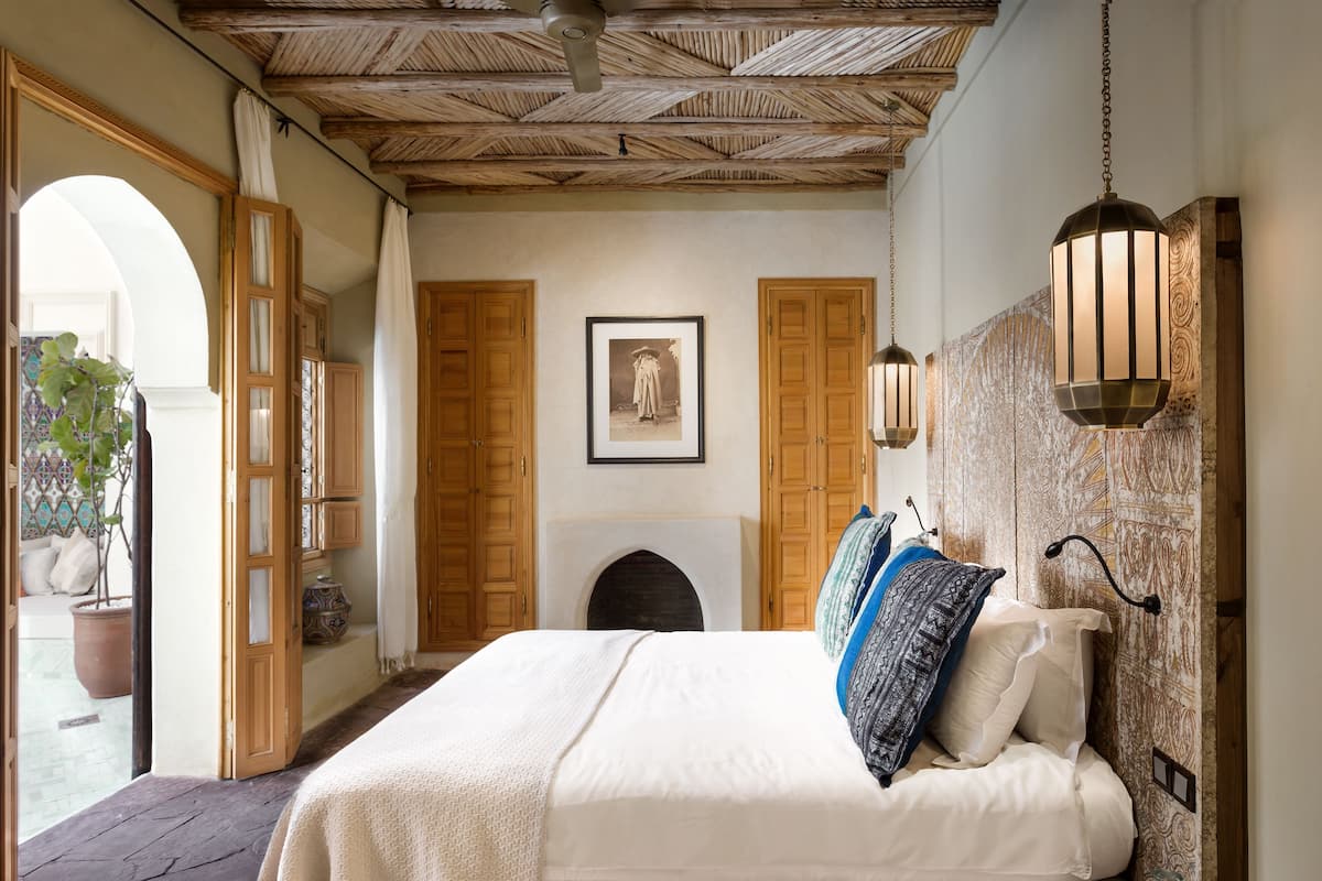 A bedroom with a large bed, wooden doors, a fireplace, and a hanging light fixture.