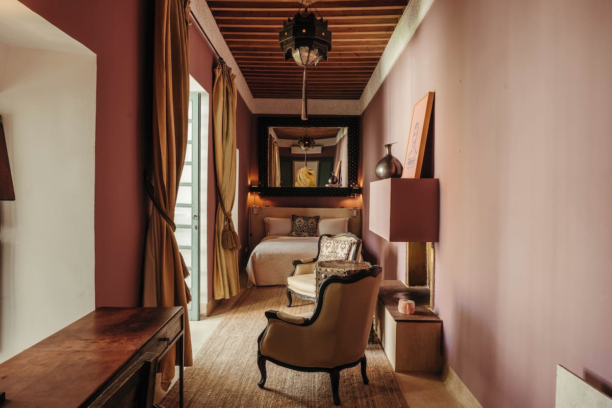 A bedroom with a bed, a chair, a bedside table, and a lamp.