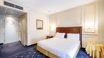 Hotelkamer met een groot bed, nachtkastje, spiegel en een wandlamp.