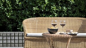 Une chaise en osier, accompagnée d’une petite table dressée pour deux personnes, avec un bol de collations et deux verres de vin rouge.