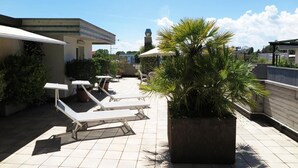 A rooftop terrace with sun loungers, a potted palm tree, and a view of the city skyline. - Numi & Medusa (Cesenatico)