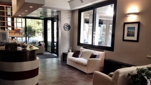 A reception area with a reception desk, a white sofa, and a large window with a view of the outdoors. - Numi & Medusa (Cesenatico)