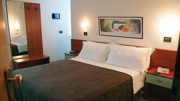 Une chambre d’hôtel avec un lit, une table de chevet, une commode, un miroir et un tableau au mur.