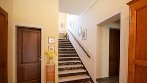 A hallway with a wooden door, a staircase with a marble finish, and a red and black patterned rug. - B&B Camere Andrei (Pienza)