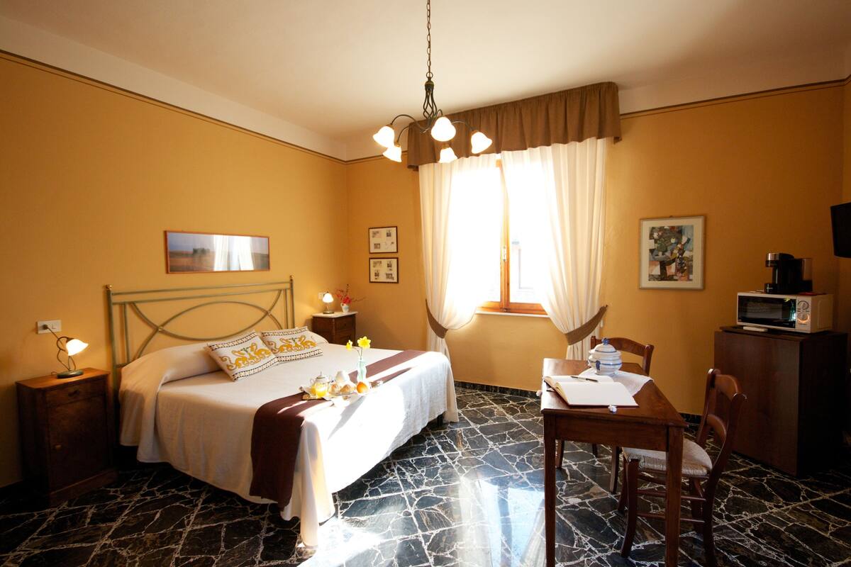 A hotel room with a bed, a desk, a chair, a television, and a window with curtains.