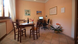 A dining area with a wooden table and chairs, a computer desk with a chair, and a potted plant. - B&B Camere Andrei (Pienza)