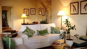 A cozy living room with a white sofa, green cushions, a coffee table, and a potted plant. There are framed pictures on the wall and a lamp on the side table. - Relais Corte Paradiso (Peschiera del Garda)