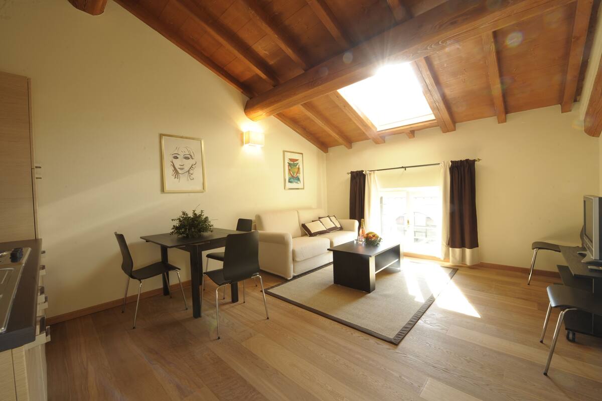 A spacious living area with a wooden ceiling, a sofa, a coffee table, and a dining table with chairs.
