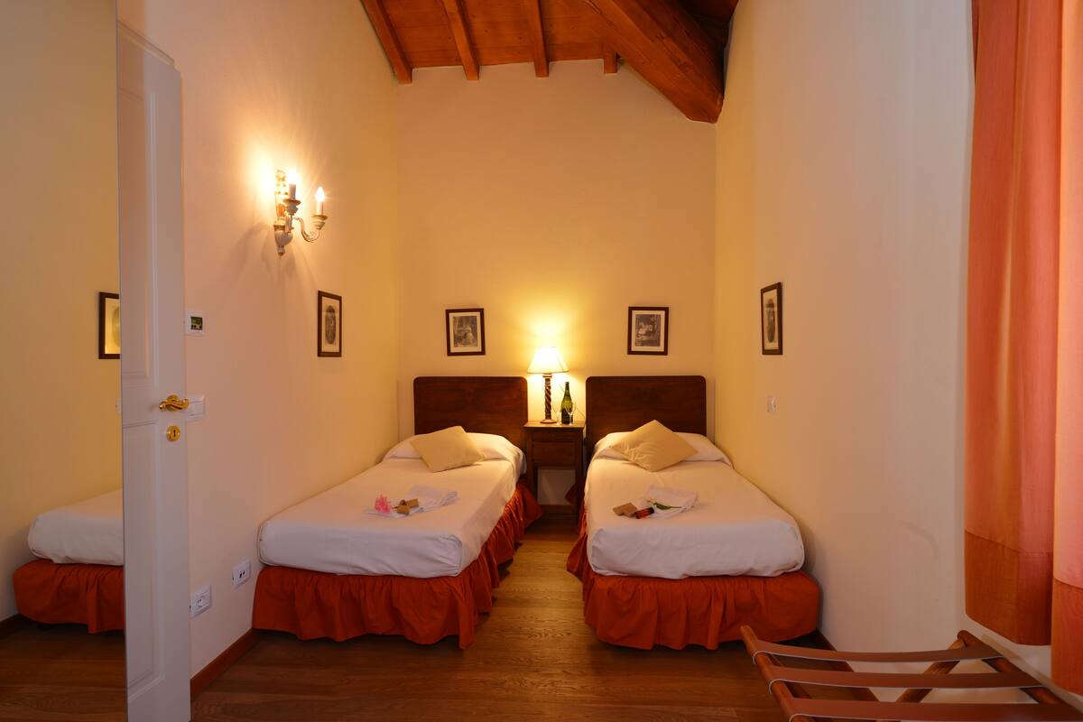 A room with two beds, wooden flooring, a wooden ceiling, and a nightstand with a lamp.