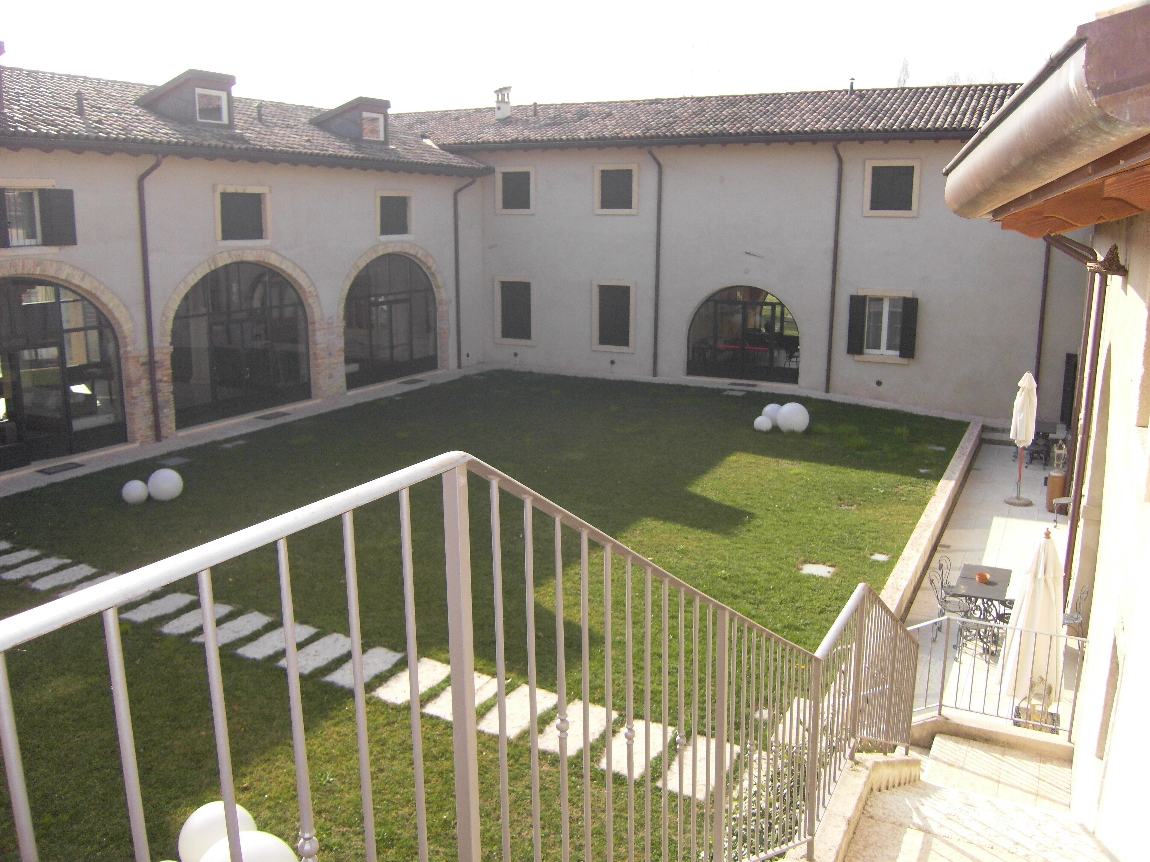 Un patio con barandilla blanca, césped y un edificio con puertas y ventanas de arco.