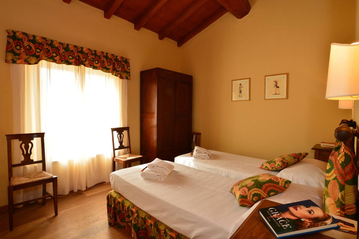 A hotel room with two beds, a wooden wardrobe, a chair, and a window with curtains.