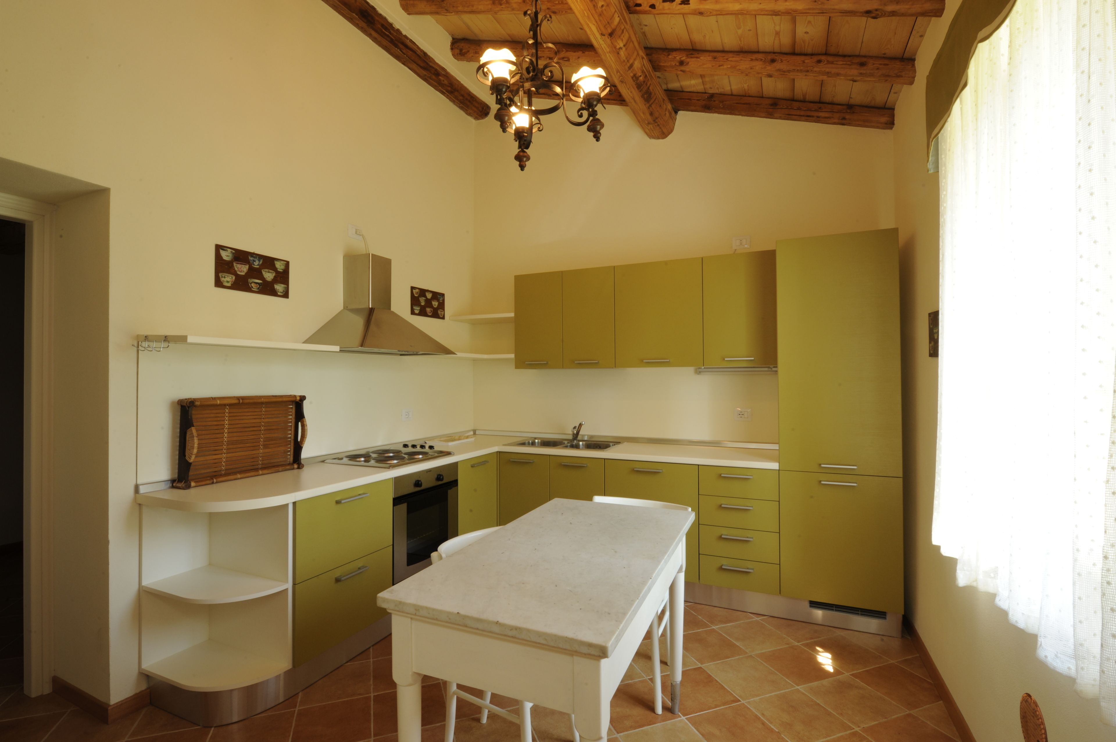 Una cocina con armarios verdes, encimera blanca y techo de madera.