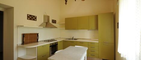 Una cocina con armarios verdes, encimera blanca y techo de madera.