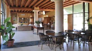A spacious lobby with high ceilings, wooden beams, and large windows. There are several wicker chairs and tables arranged for guests. - Relais Corte Paradiso (Peschiera del Garda)