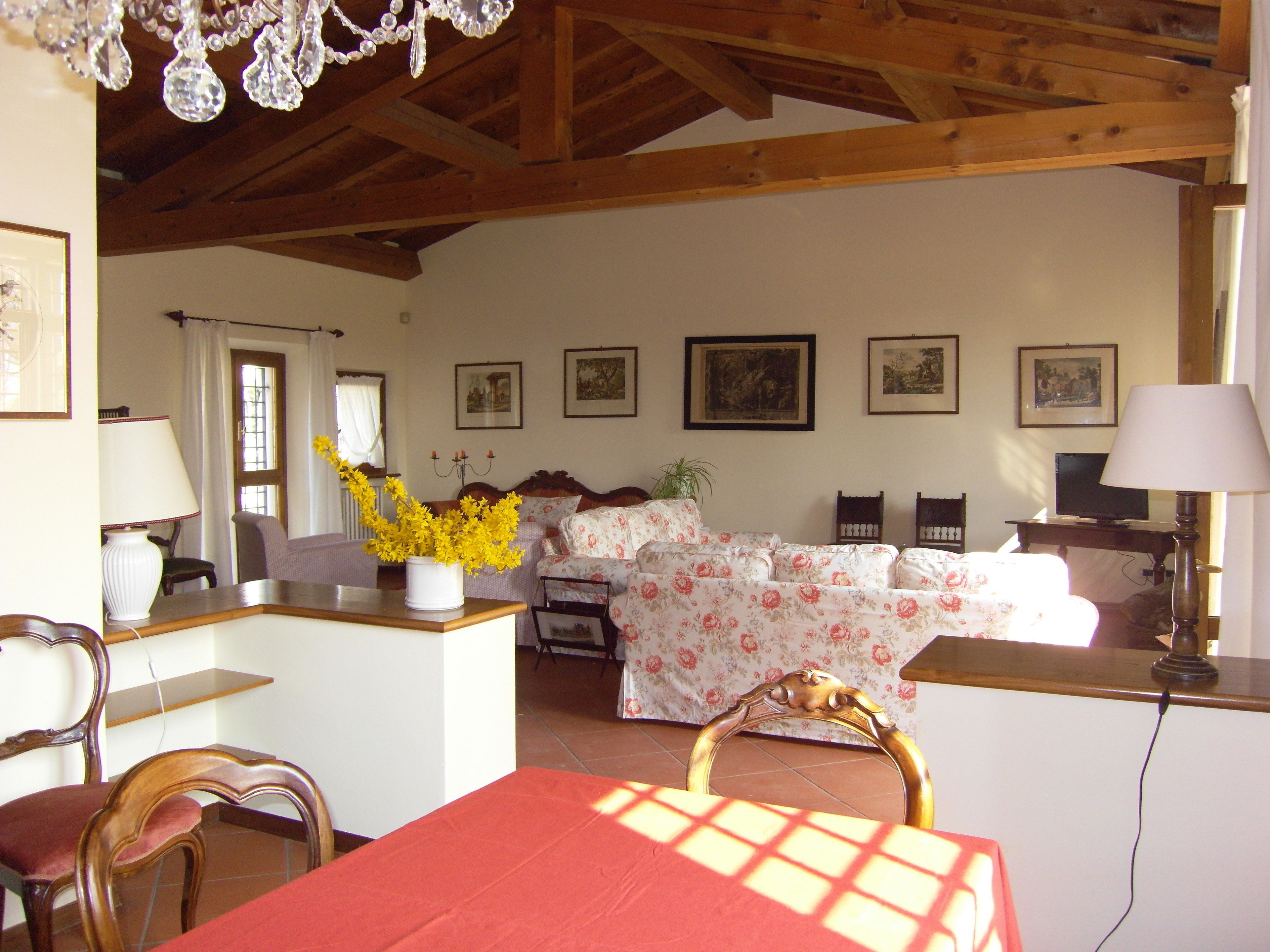 Una stanza con soffitto in legno, un tavolo da pranzo con sedie, un divano, una TV e quadri appesi alle pareti.