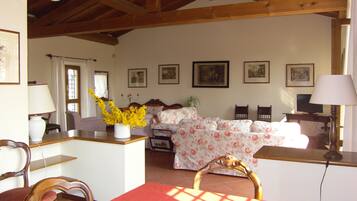 Una stanza con soffitto in legno, un tavolo da pranzo con sedie, un divano, una TV e quadri appesi alle pareti.