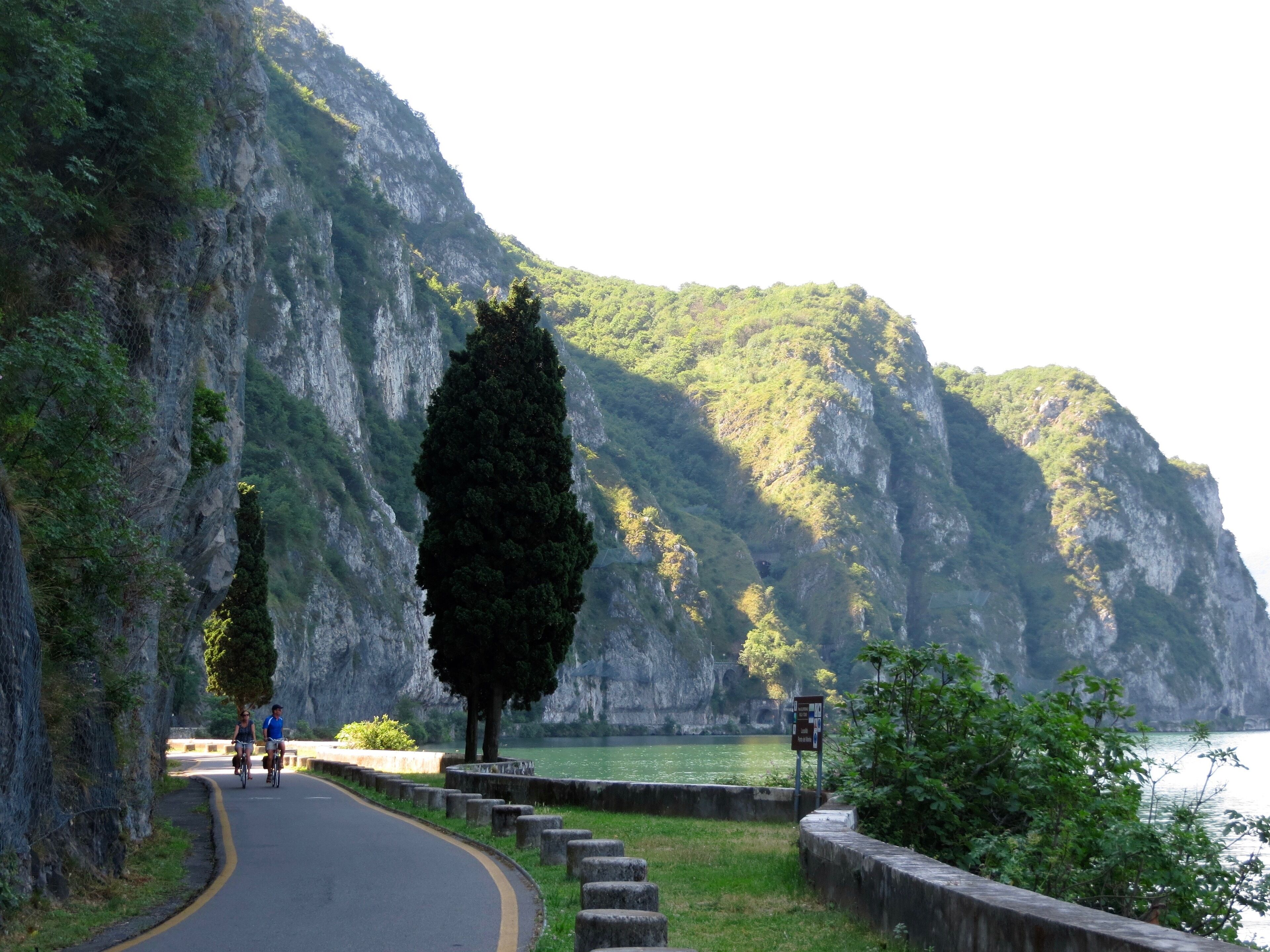 A paved road curving alongside a cliff with a body of water in the background.