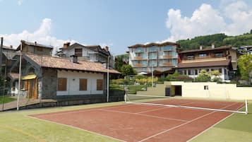 A tennis court with a net in the middle, surrounded by buildings with balconies and a stone wall.
