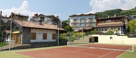 A tennis court with a net in the middle, surrounded by buildings with balconies and a stone wall.