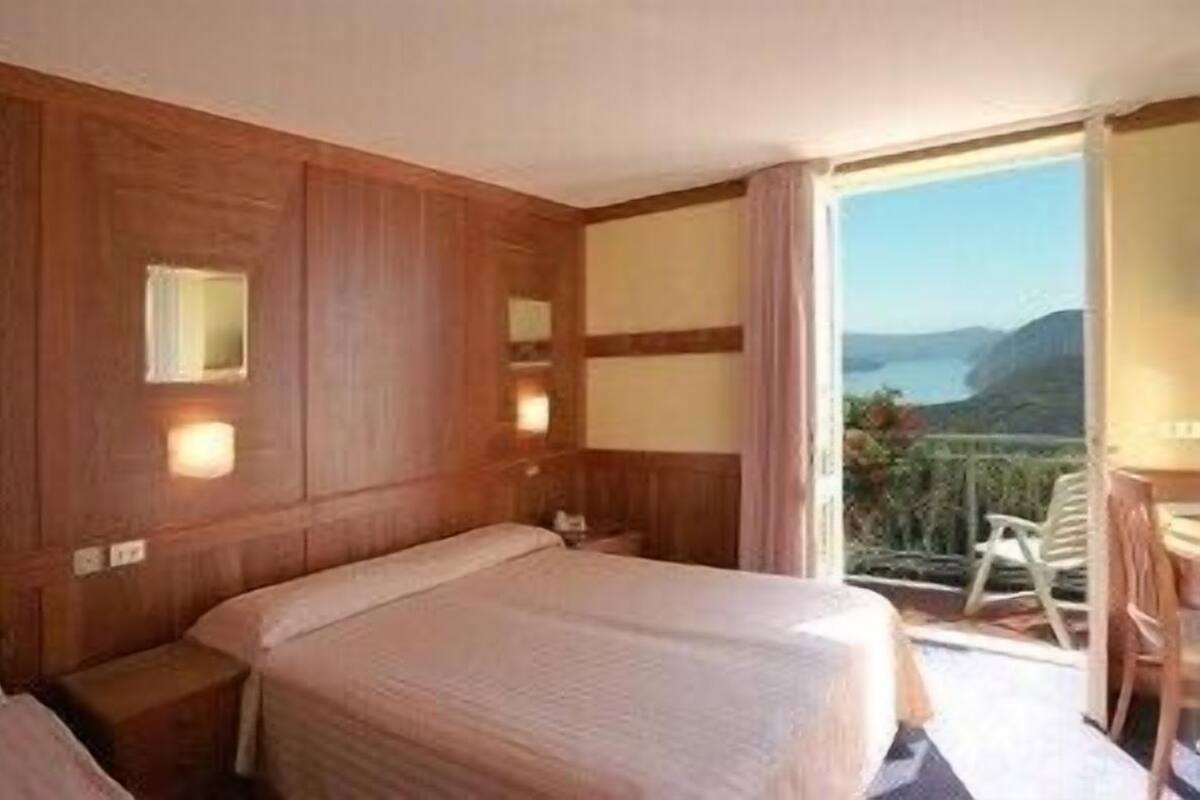 Habitación de hotel con pared de paneles de madera, una cama grande, una mesita de noche y vistas al exterior.