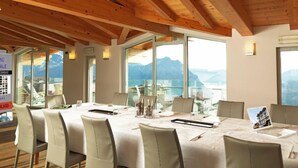Un salón de conferencias con una mesa grande, sillas y vistas a montañas a través de amplios ventanales.