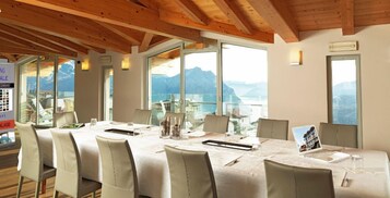 Un salón de conferencias con una mesa grande, sillas y vistas a montañas a través de amplios ventanales.