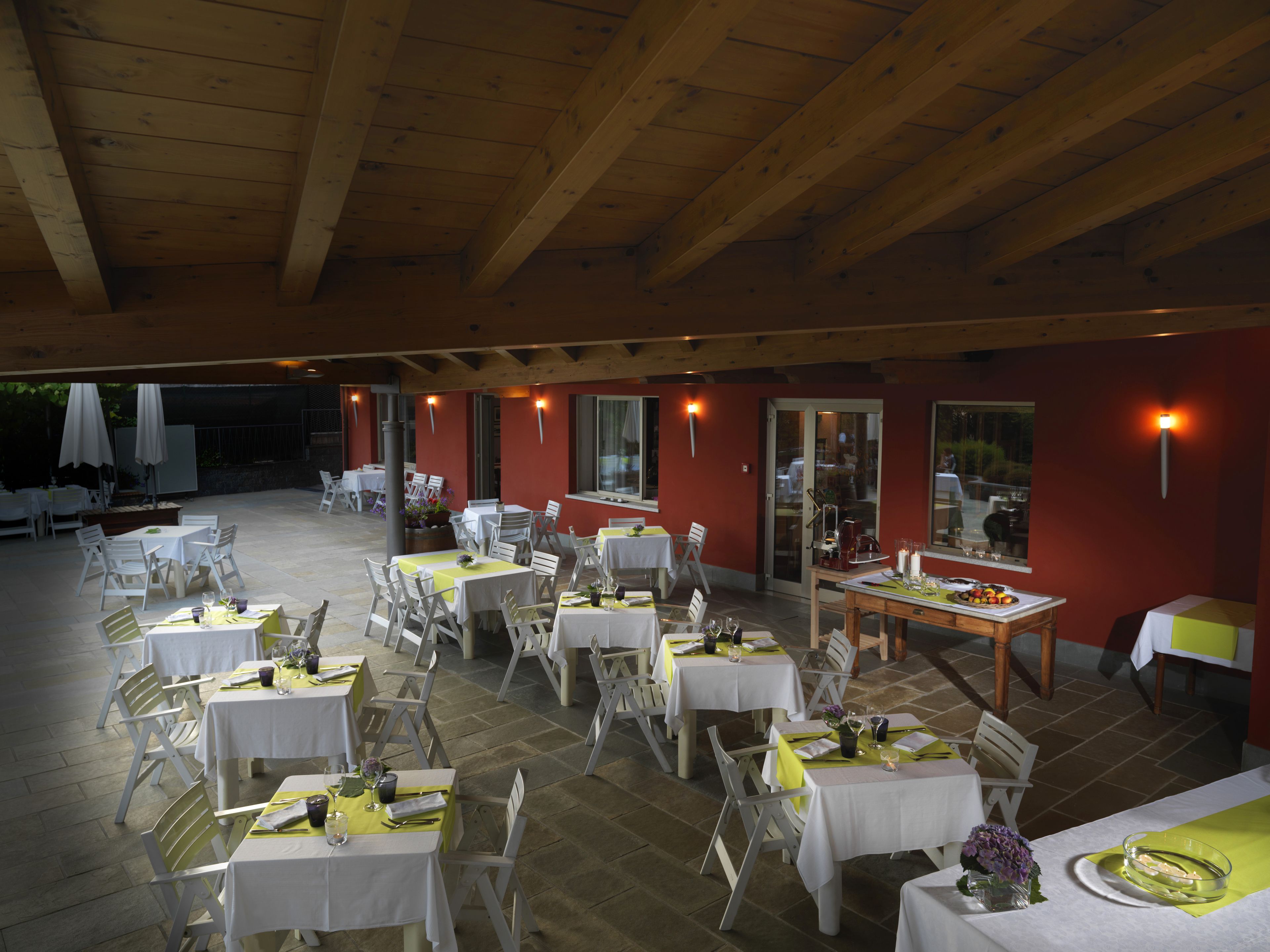 Ein Außenbereich zum Essen mit mehreren Tischen und Stühlen, Holzbalken an der Decke und einer roten Wand.