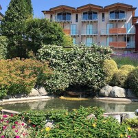 Un edificio moderno con varios balcones y un jardín bien cuidado con un estanque.