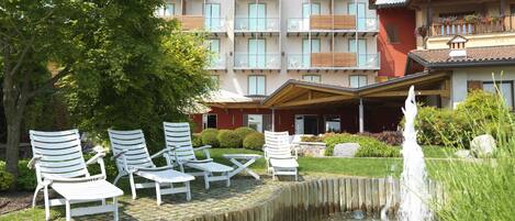 A hotel with a pool, lounge chairs, and a fountain.