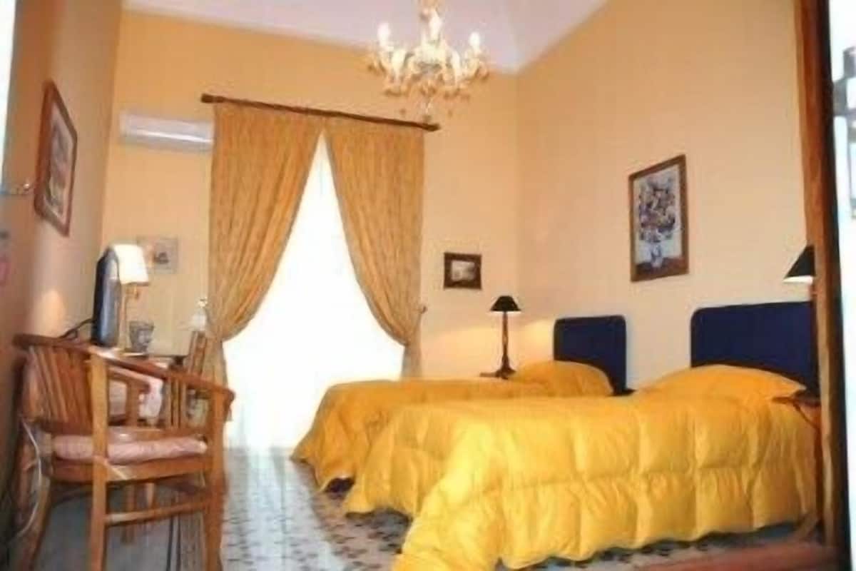 Hotellihuone, jossa on kaksi sänkyä, työpöytä, tuoli ja kattokruunu.