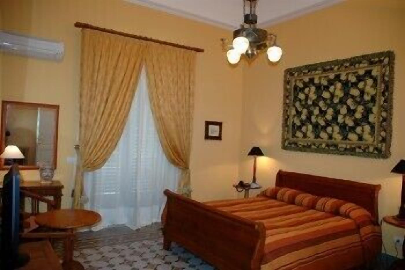 Um quarto com uma cama, duas luminárias de cabeceira, um espelho, uma mesinha e uma janela com cortinas.