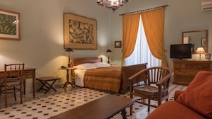 Quarto de hotel com uma cama, uma cadeira de madeira, um sofá, uma mesinha, uma televisão e um quadro na parede.