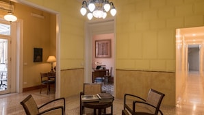 Um hall com piso xadrez, um candelabro e uma mesa com cadeiras.