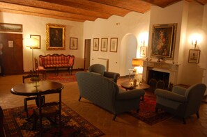 Ein traditionell eingerichtetes Wohnzimmer mit einem roten Sofa, zwei Sesseln, einem runden Tisch und einem Kamin.