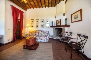A cozy living room with a floral sofa, a fireplace, and a collection of framed pictures on the wall.