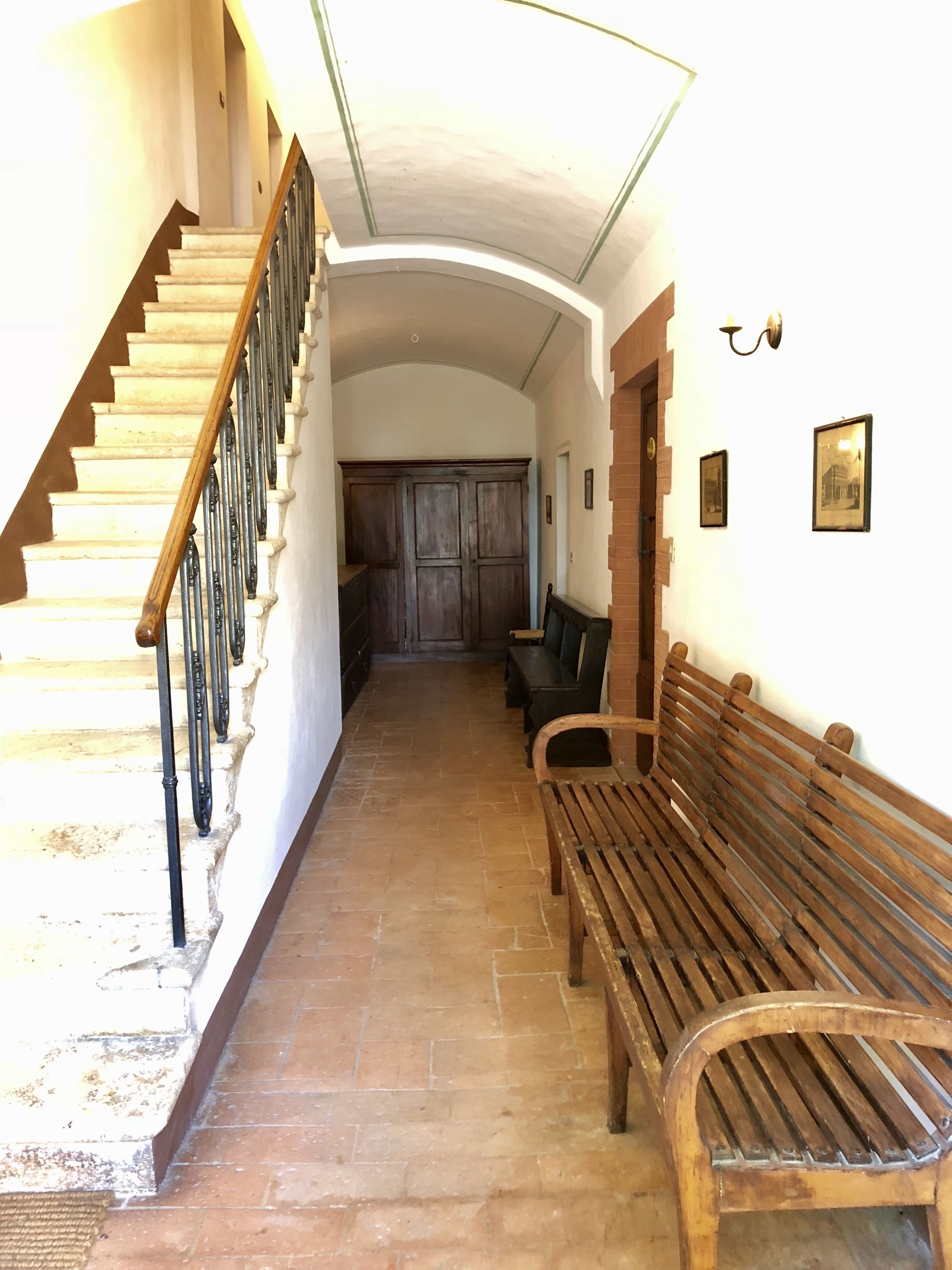 Un pasillo con una escalera de madera, un banco y una puerta que da a otra habitación.