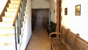 Un pasillo con una escalera de madera, un banco y una puerta que da a otra habitación.