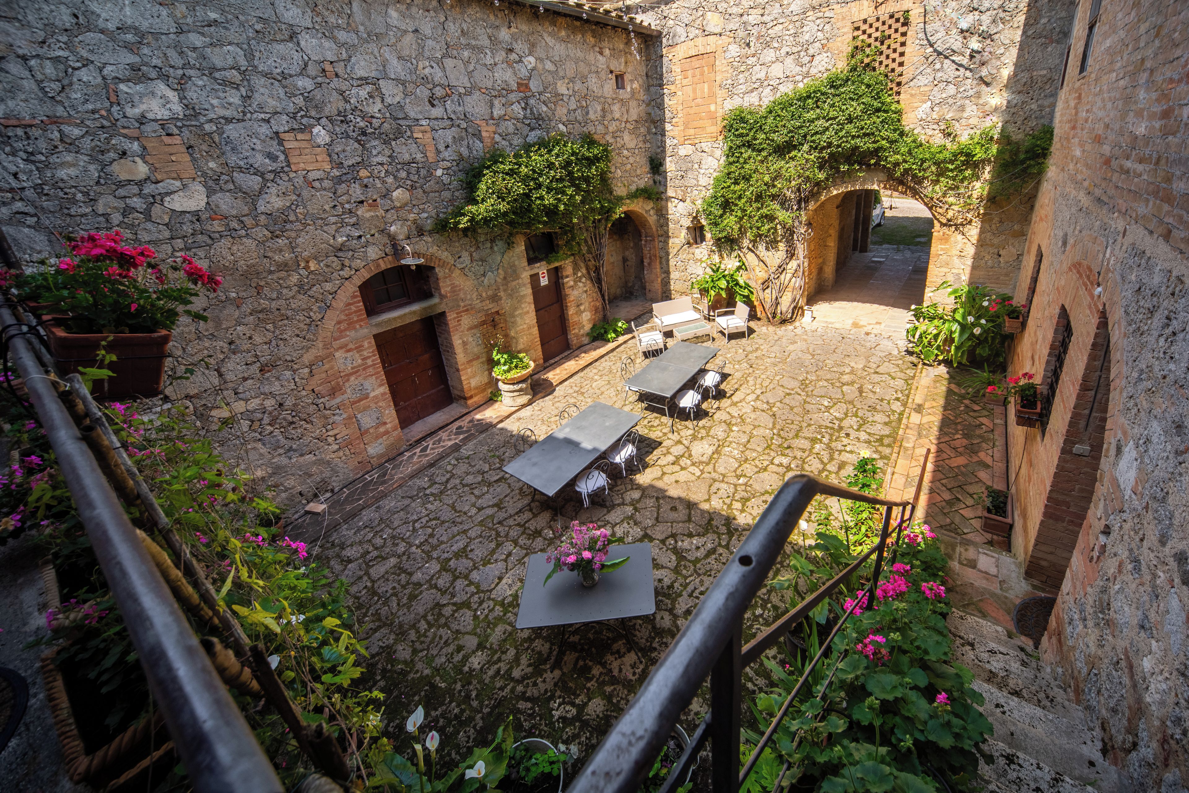 Un patio con muros de piedra, una zona de estar con mesas y sillas, y plantas en macetas.
