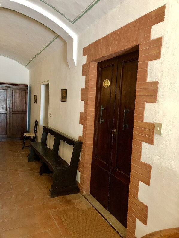 A hallway with a wooden bench, a door with a brass handle, and a tiled floor.