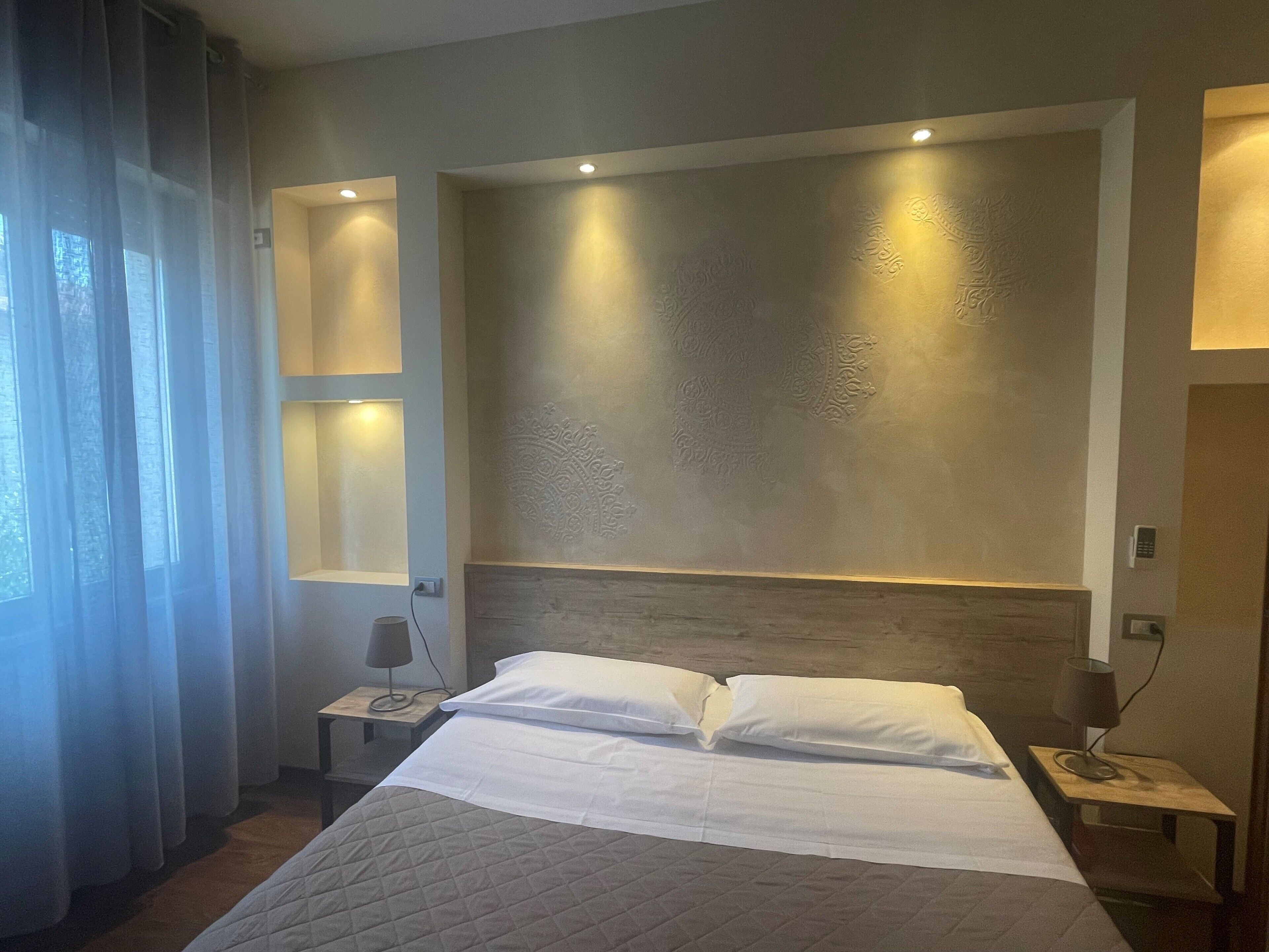 Habitación de hotel con una cama grande, lámparas de noche y una pared con diseño texturizado.