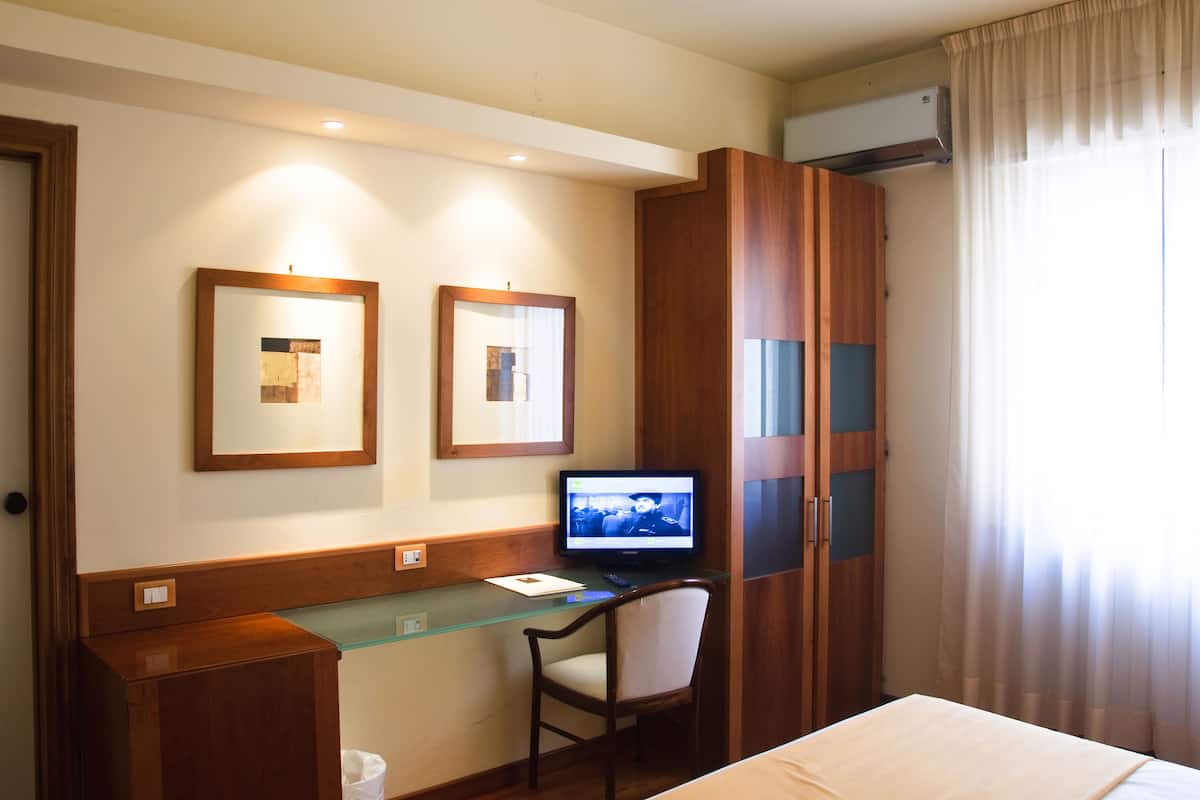 A hotel room with a wooden desk, a chair, a bed, and two framed pictures on the wall.