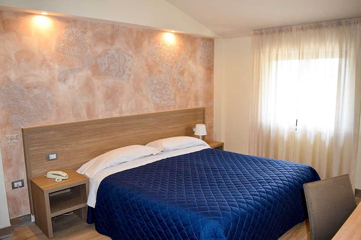 A hotel room with a large bed, a bedside table with a lamp, and a telephone.
