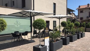 An outdoor seating area with tables and chairs under umbrellas, surrounded by potted plants. - Hotel Le Grazie (Assisi)